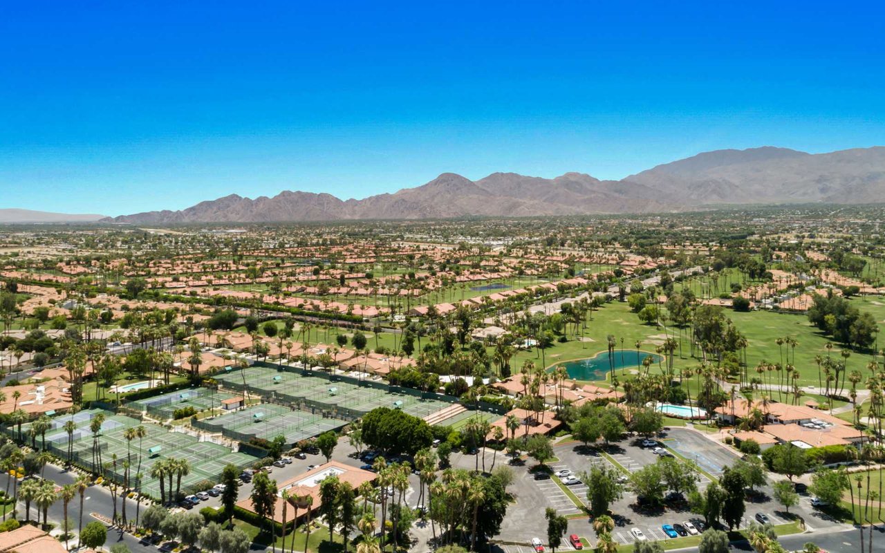 a sprawling complex with a golf course, tennis courts, and numerous buildings surrounded by palm trees