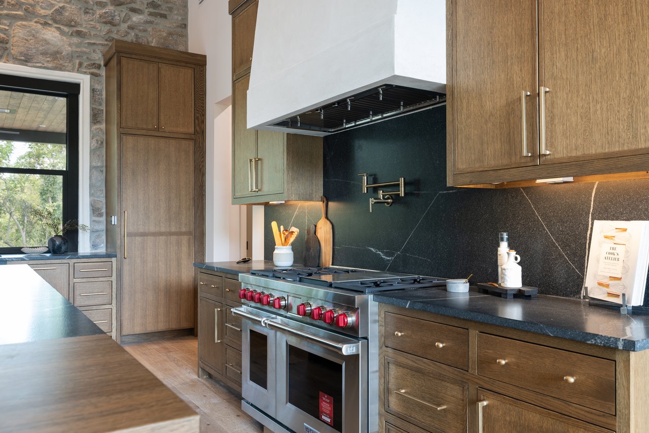 Kitchen with a stainless-steel range, red knobs, dark stone backsplash, and warm wood cabinetry.