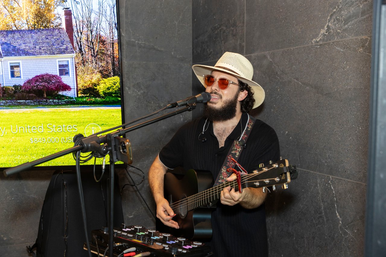 A bearded guitarist in a straw hat and sunglasses performs into a microphone.