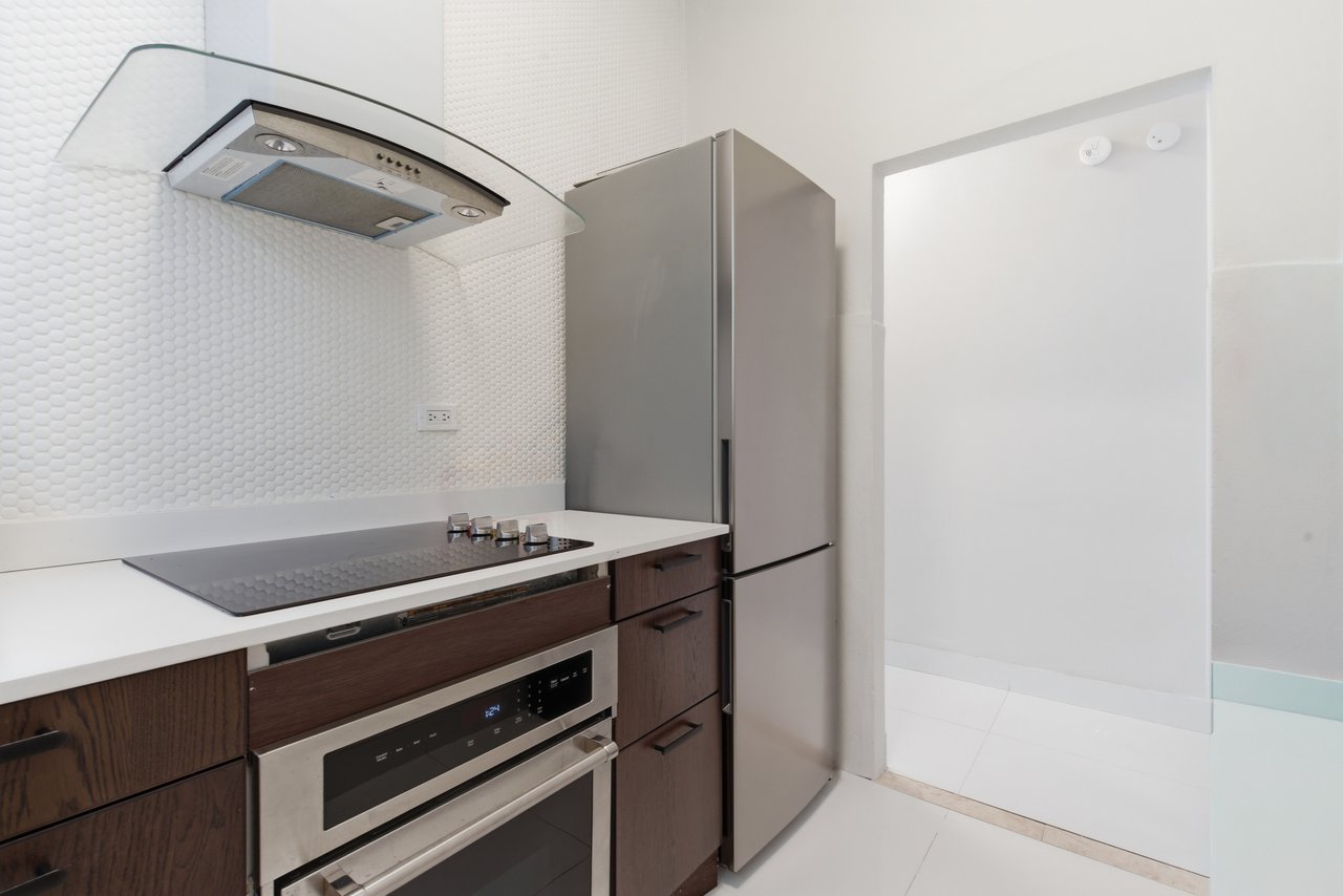 Modern kitchen with dark wood cabinets, a stainless steel cooktop and oven, and a tall refrigerator.