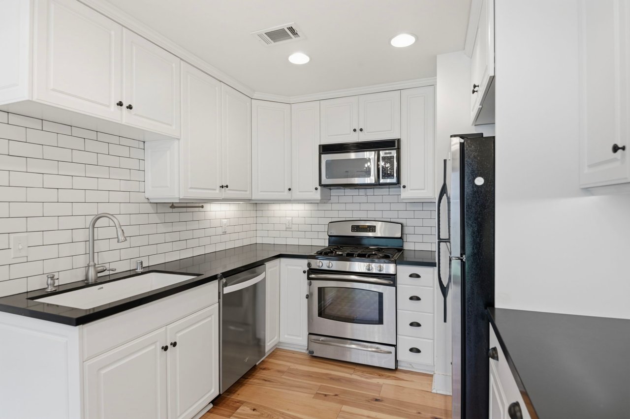 Kitchen with gas range, built-in microwave, stainless steel refrigerator, and ample white cabinetry with dark counters