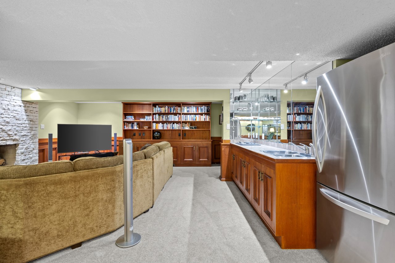 Basement media room with built-in wood bookcases, tan sectional seating, and a long wet bar.