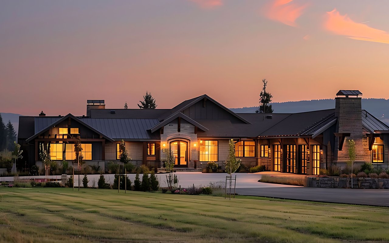 Ranch-style residence with glowing windows, stone chimneys, and landscaped grounds at dusk.