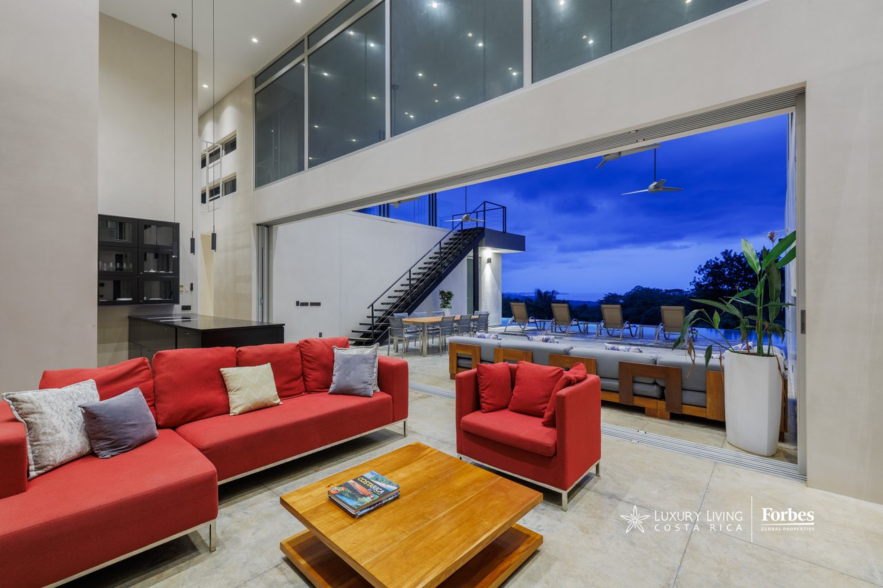 Double-height living room with red sofas opening onto a furnished terrace at dusk.