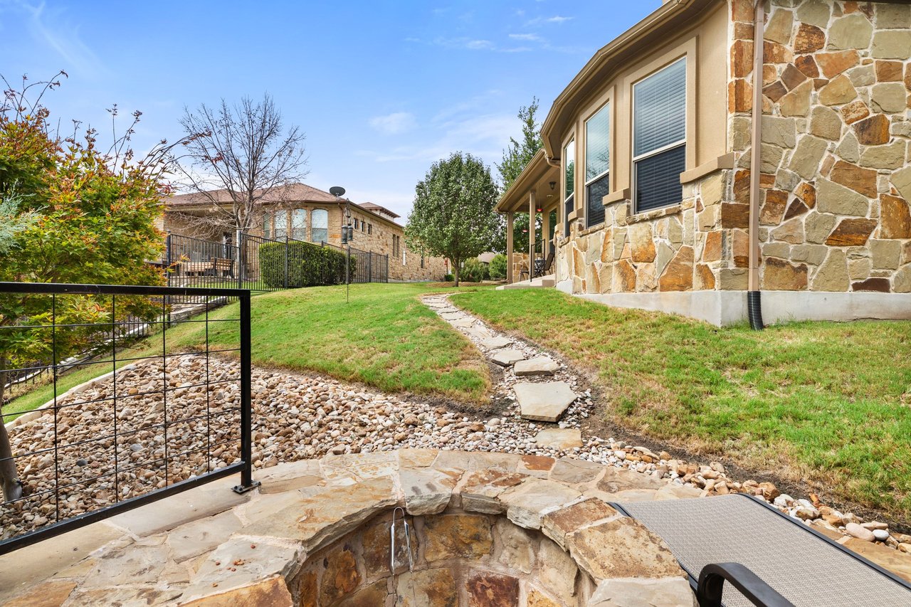 Stone-sided home and landscaped backyard with a flagstone path, rock garden, and raised stone spa.
