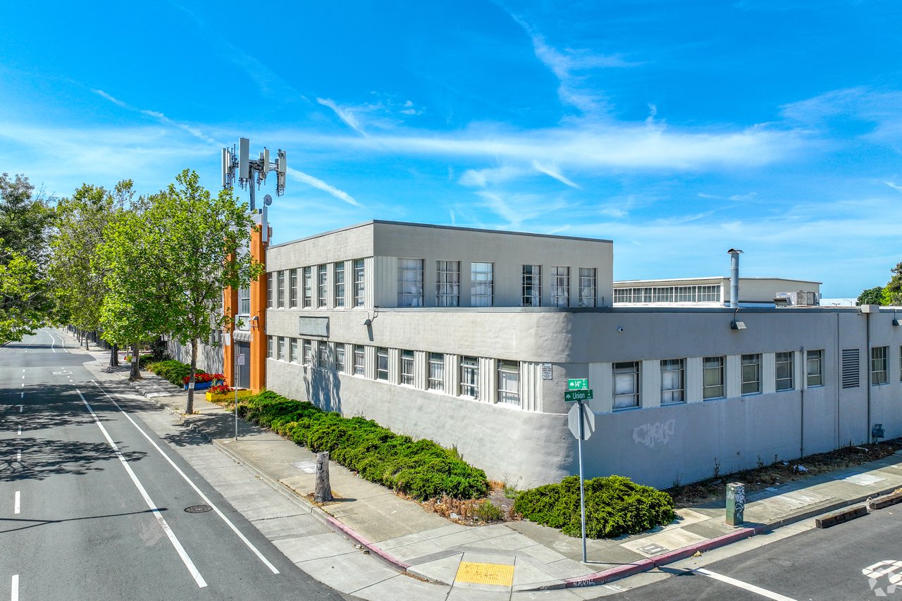 Gray commercial building on a street corner, with rows of windows and a cellular antenna array.