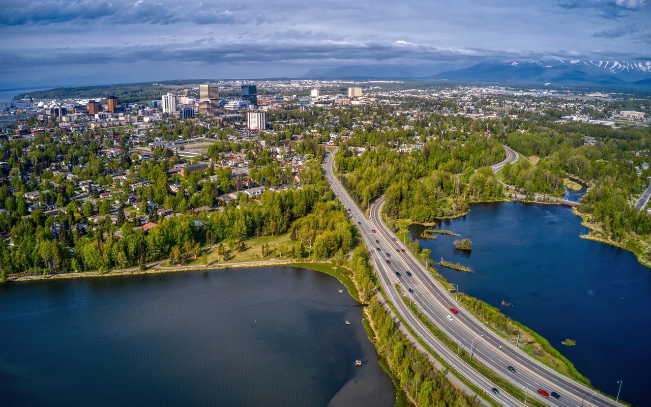 Aerial view of Anchorage beside lakes, with downtown and mountains beneath cloudy skies.