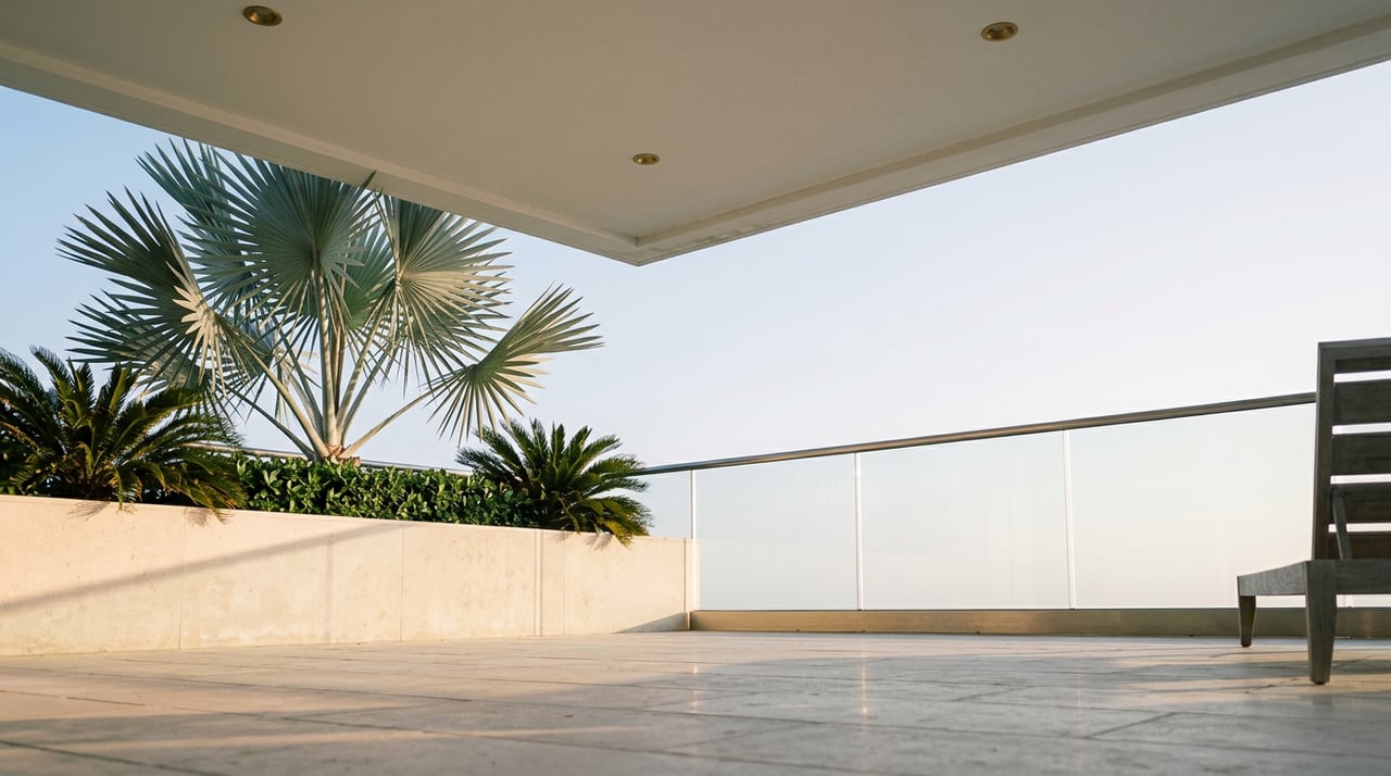 Low limestone terrace with a silver-blue fan palm, glass railing, and shaded white balcony soffit.