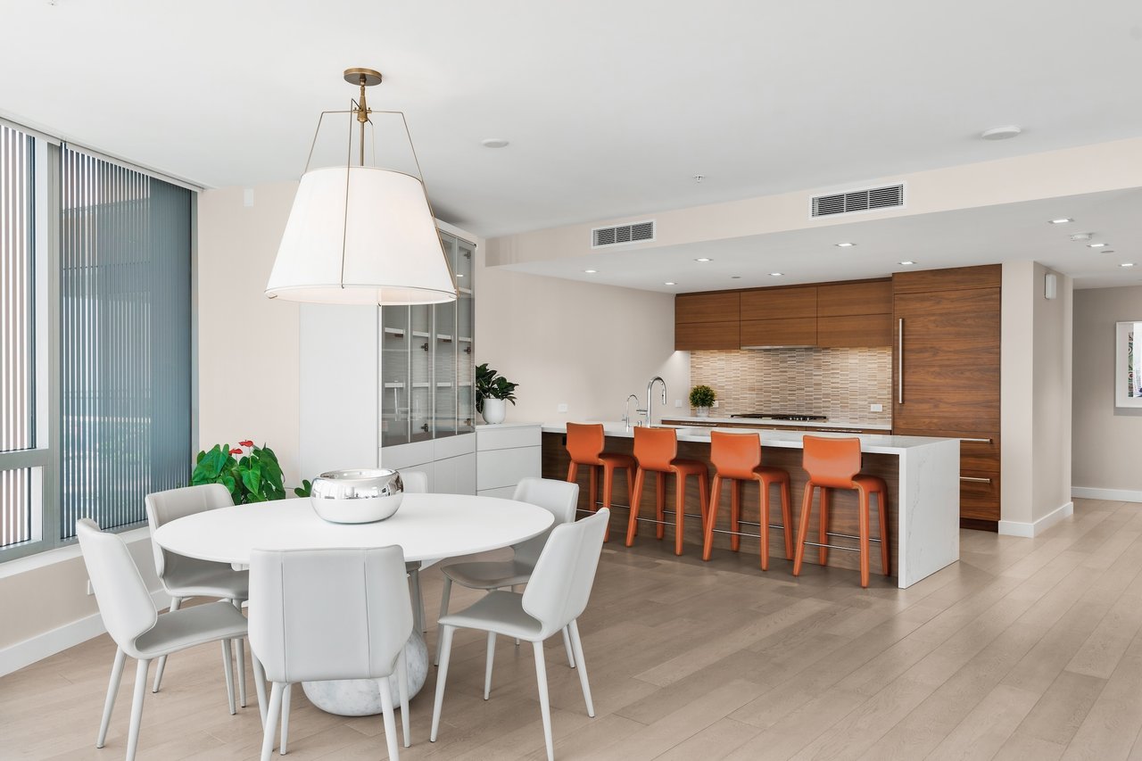 Open-plan kitchen and dining area with walnut cabinets, orange bar stools, and a round white dining table.