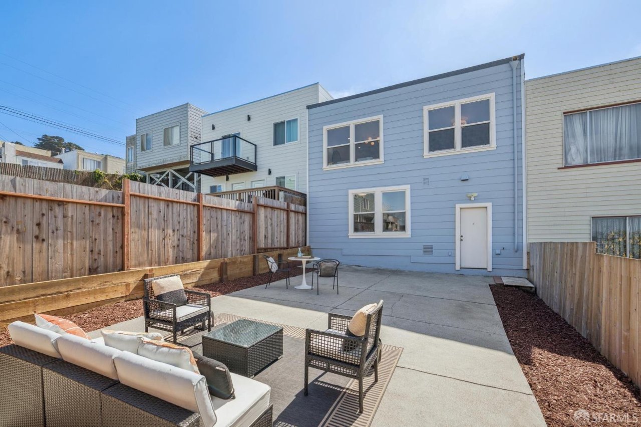 Rear patio with outdoor lounge seating, dining set, and fenced concrete yard beside a blue-sided home.