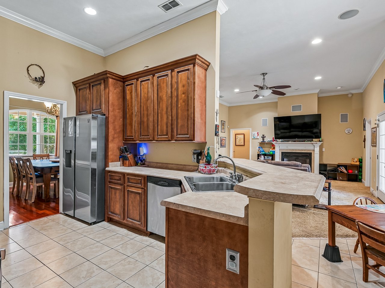 Kitchen with dark wood cabinets and a large peninsula opening to a living room with fireplace.