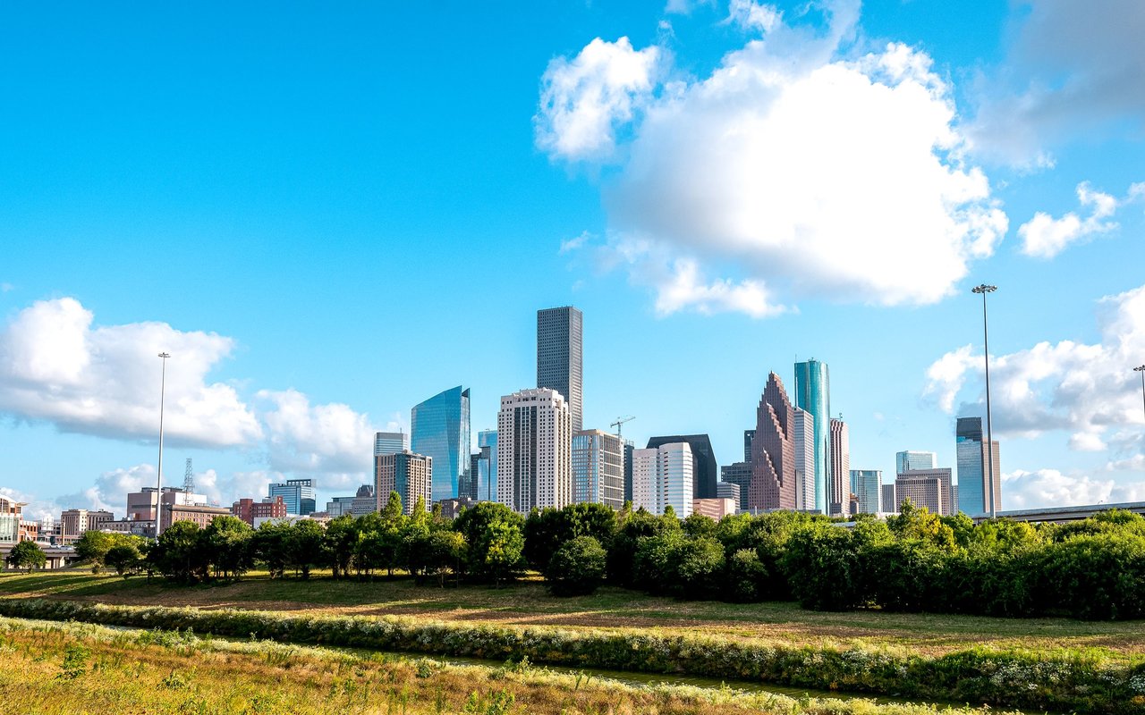 Houston skyline beyond a green park under a bright, cloud-filled sky.