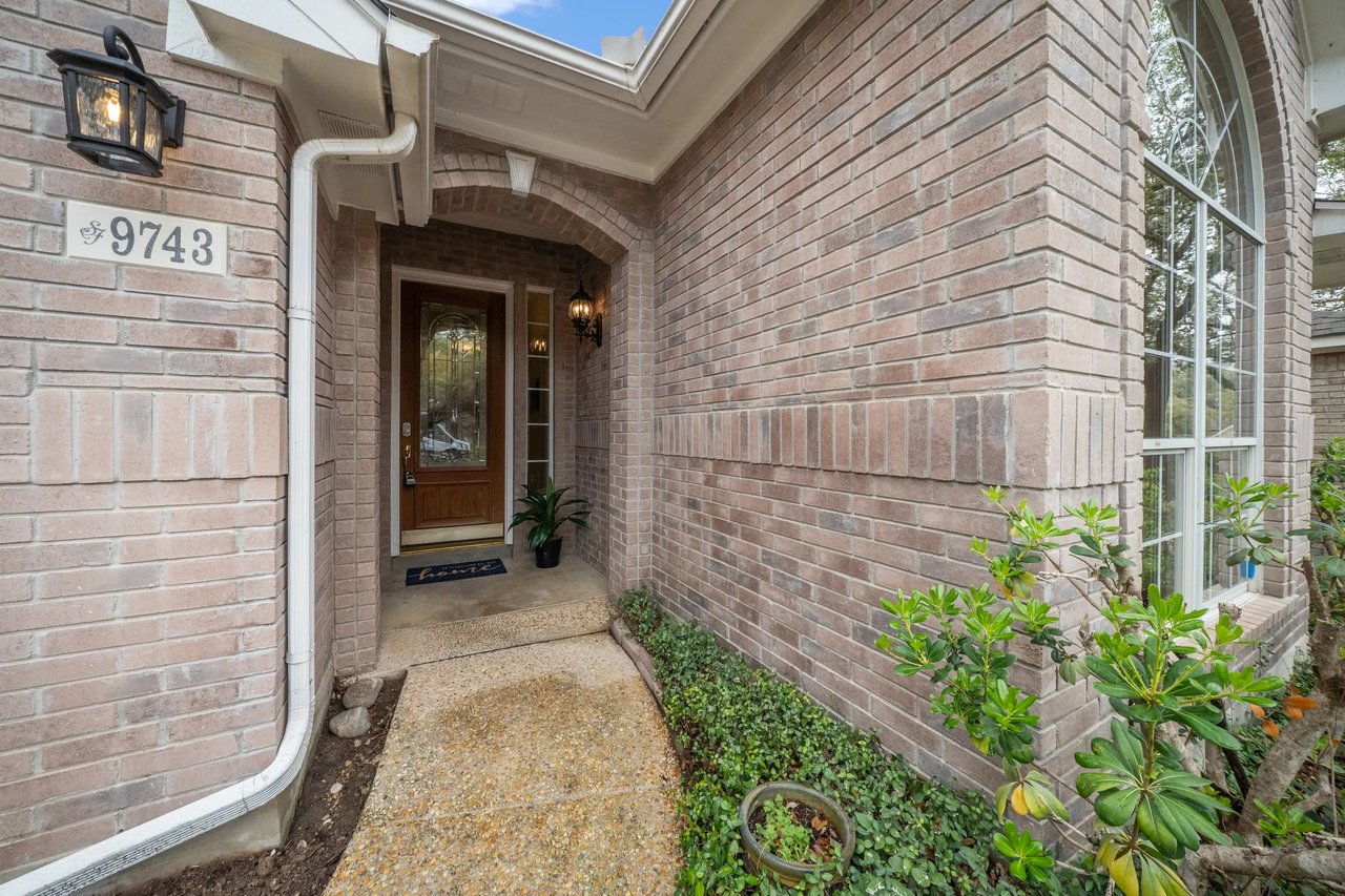 Brick home entrance with an arched porch, wooden front door, and address 9743.