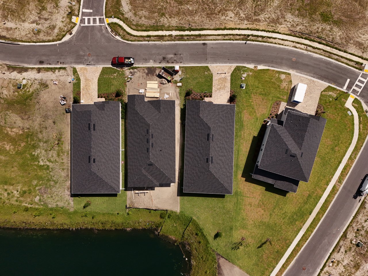Aerial view of newly built homes beside a pond and neighborhood streets.