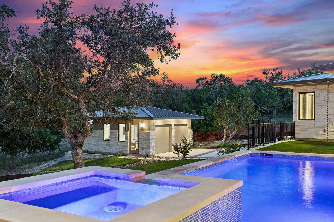 Twilight backyard pool and spa beneath a mature oak tree at this Caudill Lane home in the Bee Caves area of Austin, Texas.