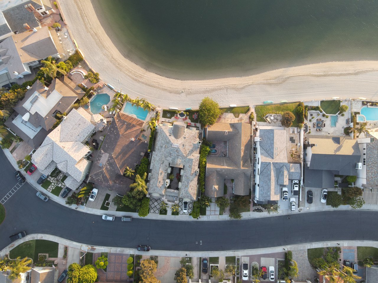 Aerial view of waterfront homes and pools along a sandy beach.