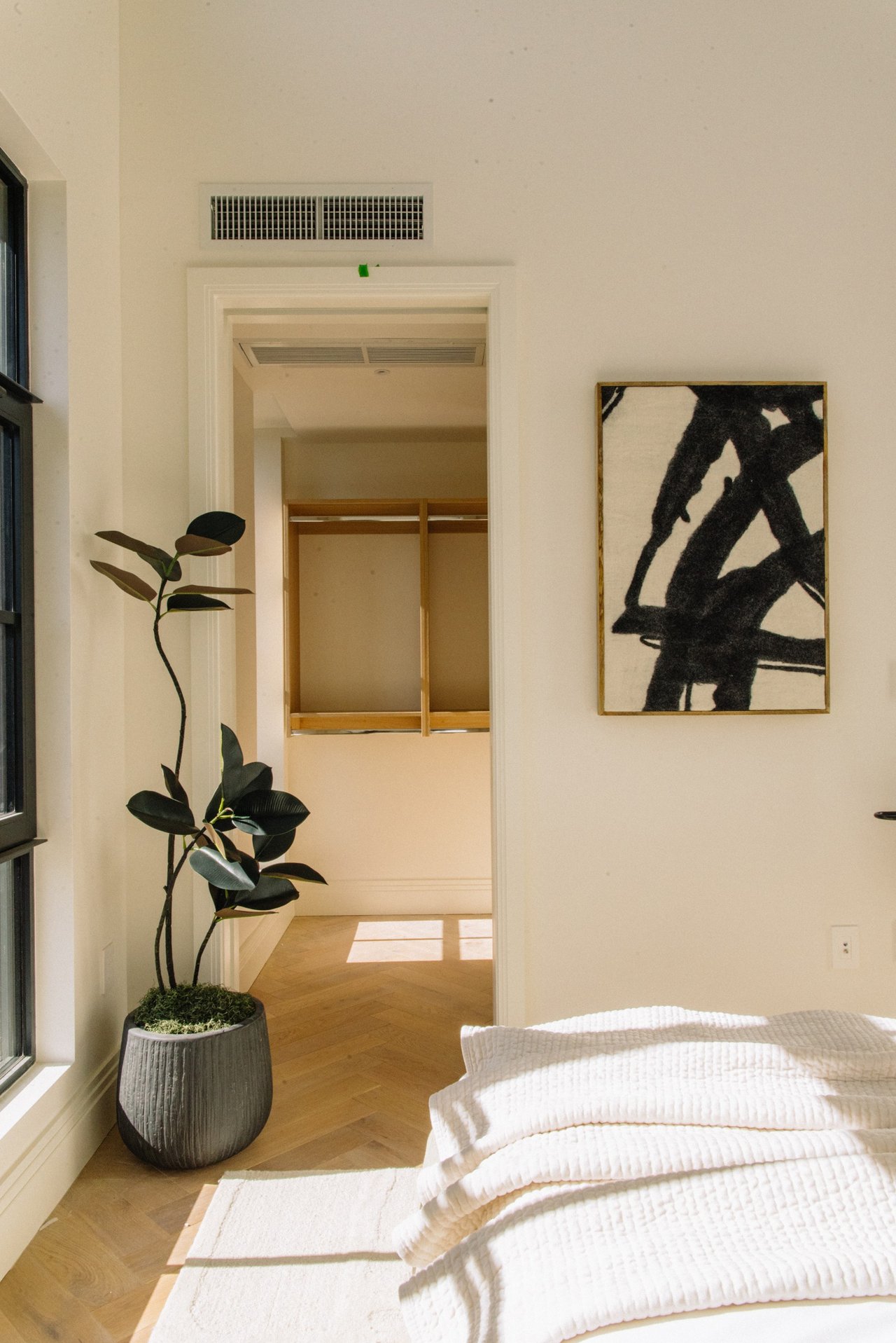 Bright bedroom with a white quilted bed, potted plant, and doorway to a closet.