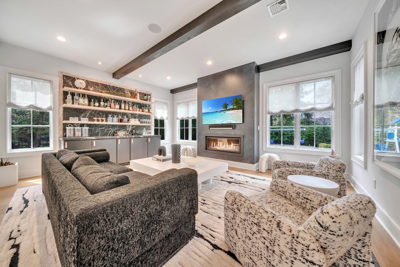Living room with a built-in bar, linear fireplace, vaulted ceiling, and large windows.