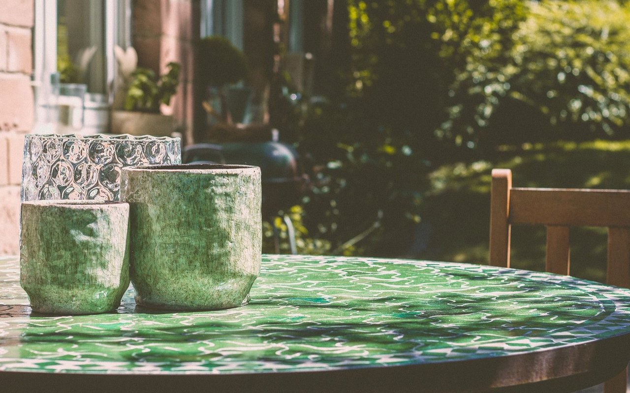 Ceramic vessels on a green mosaic table in a leafy garden.