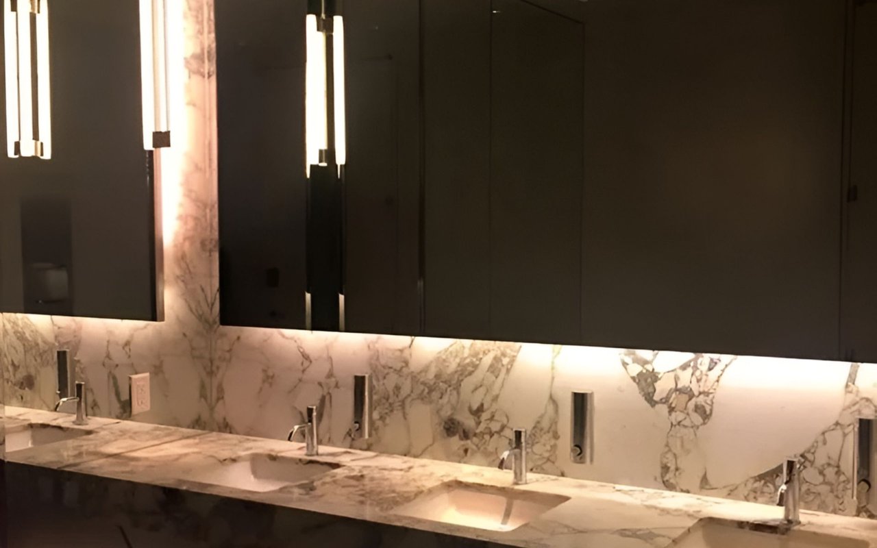 Hotel bathroom vanity with veined marble counters, multiple sinks, and dark cabinetry.