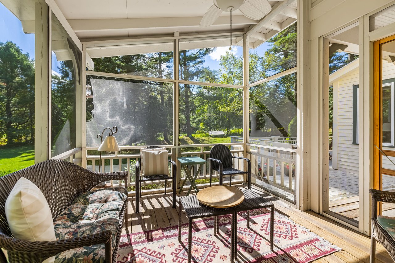 Screened porch with wicker seating and a patterned rug overlooking a leafy lawn.