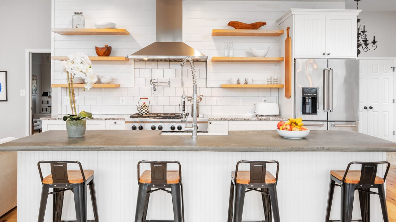 Bright white kitchen with a concrete-topped island, wood shelves, and stainless steel appliances.