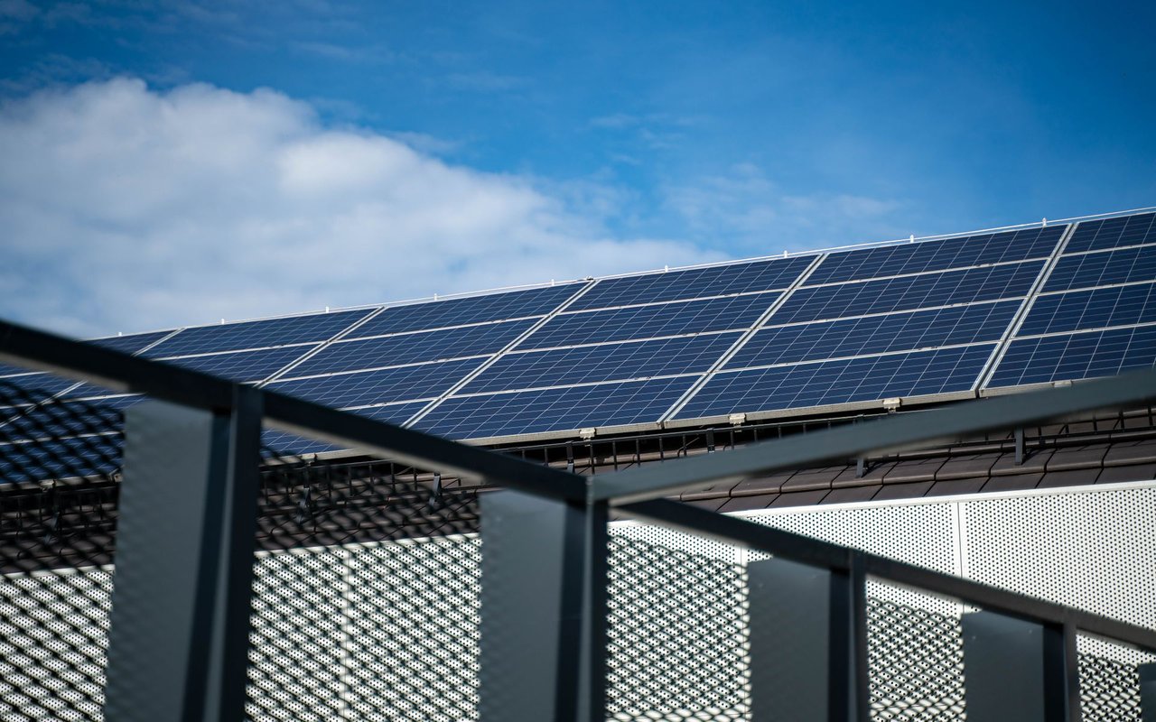 Rooftop solar panels on a modern building beneath a partly cloudy blue sky.