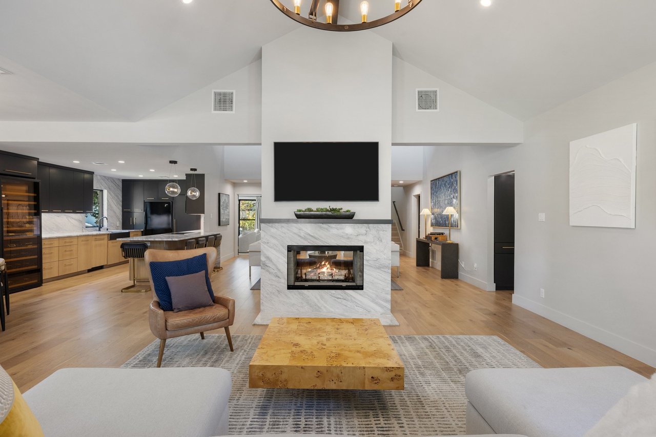 Open-plan living room with vaulted ceiling, marble fireplace, and dark kitchen cabinetry.