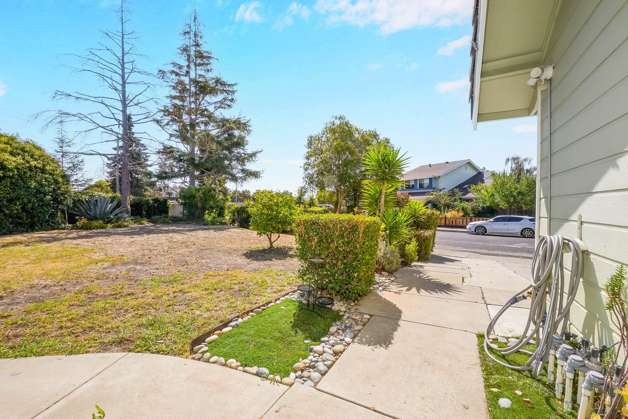 Front yard with a broad lawn, stone-edged garden bed, shrubs, and walkway to the street.