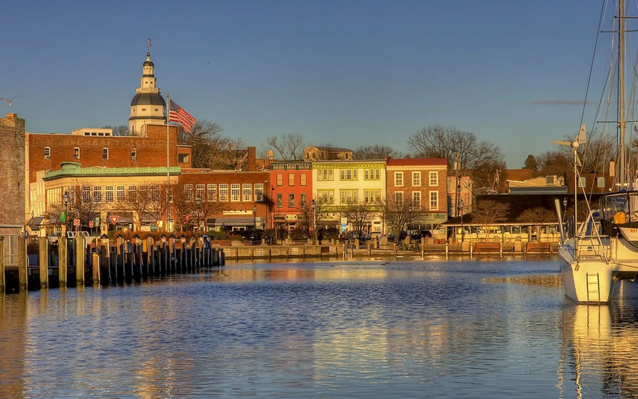 Annapolis harbor with docked boats and the Maryland State House dome above colorful waterfront buildings.