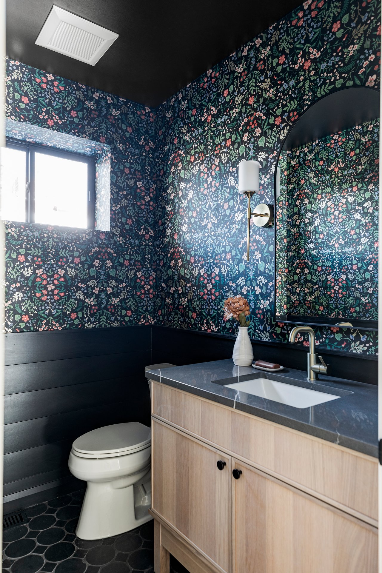 First-level bathroom with eccentric floral wallpaper, black wood paneling and black tile