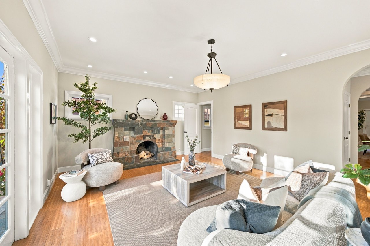 Living room with a stone fireplace, hardwood floors, and neutral seating.