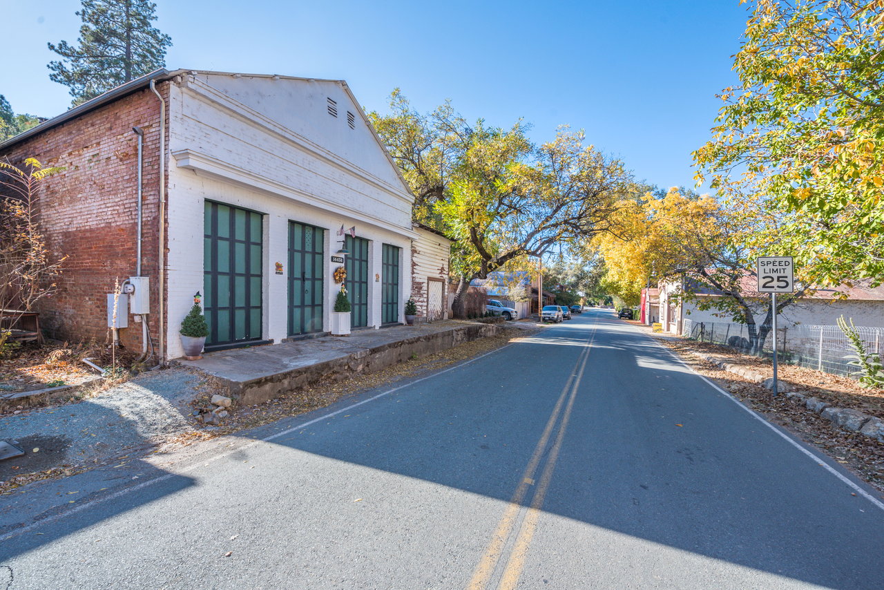Quiet street with a white brick storefront, autumn trees, and a 25 mph speed limit sign.