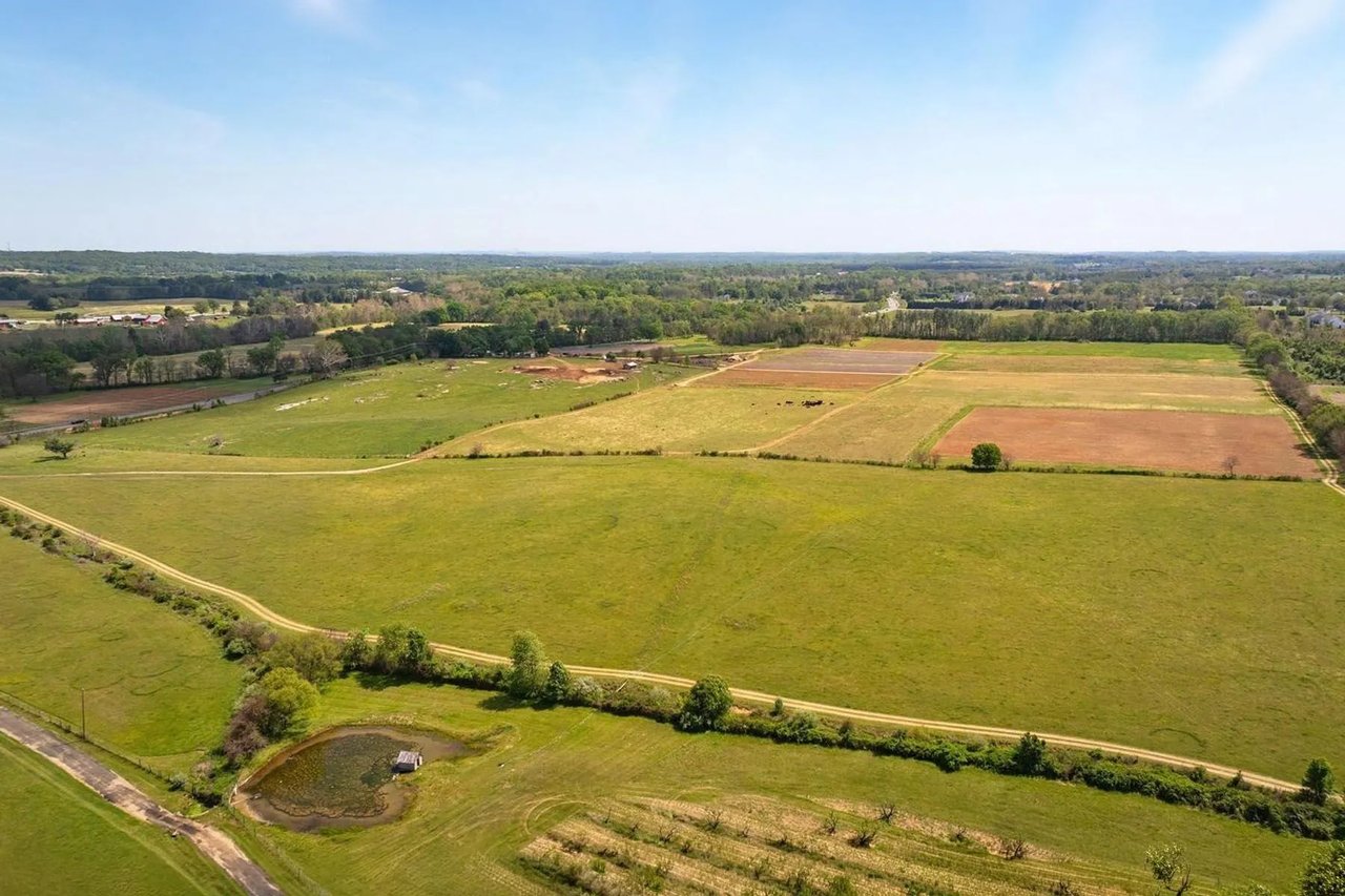 Aerial view of expansive fields and farm tracks, with a small pond in the foreground.