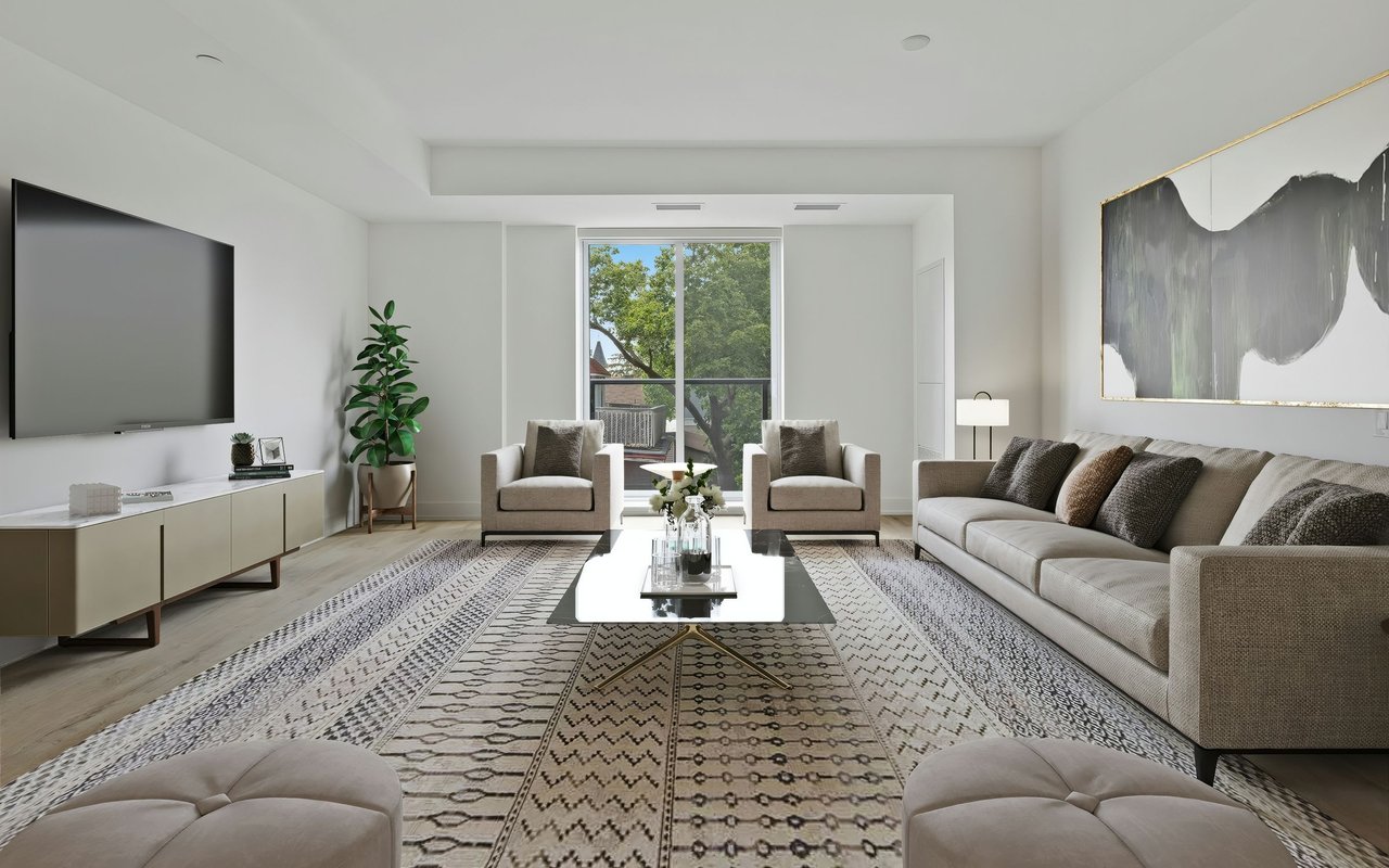 Staged living room with a large sectional, patterned rug, and tall windows overlooking trees.