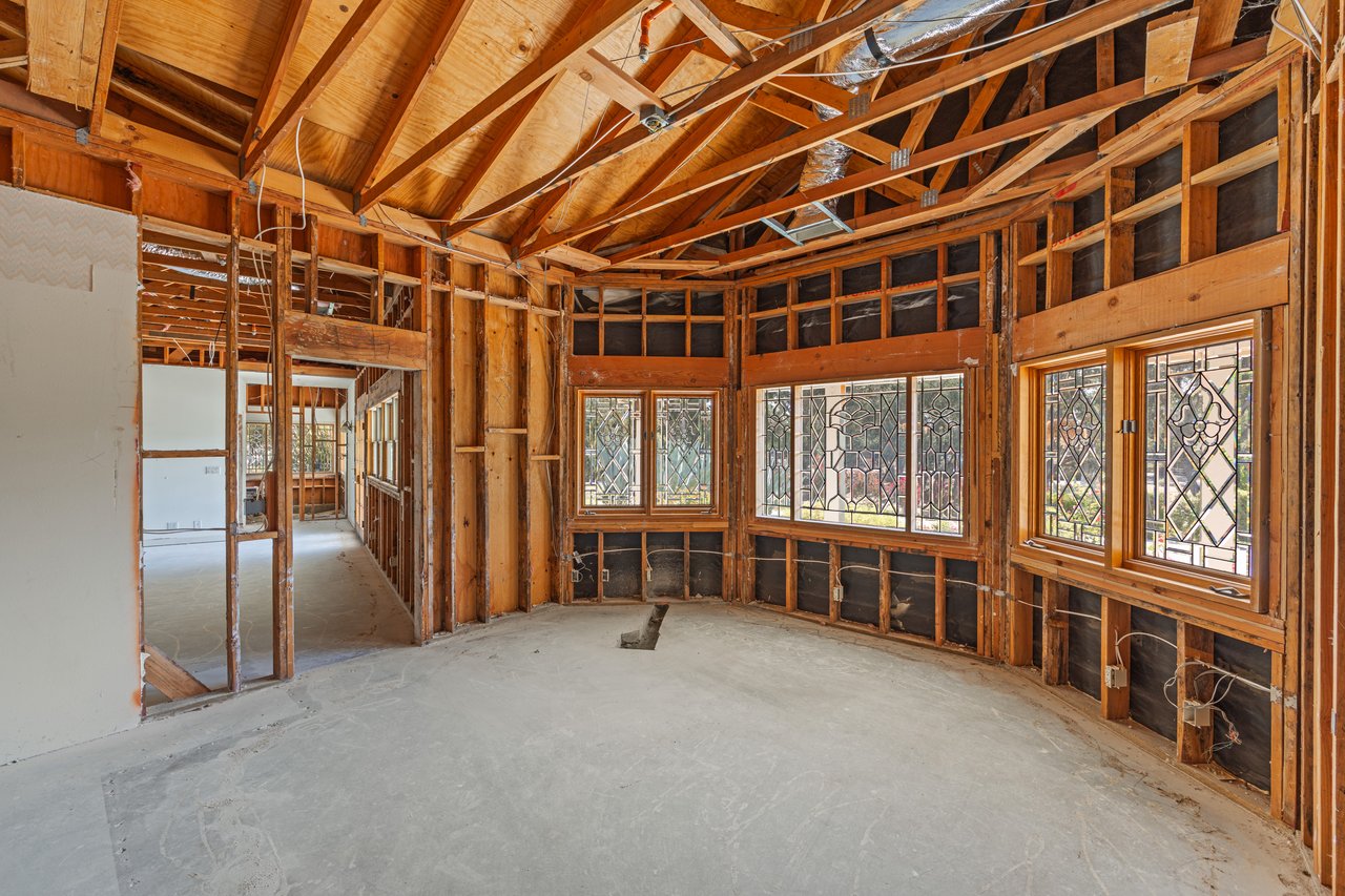 Unfinished room with exposed timber framing, concrete floor, and decorative leaded-glass windows.