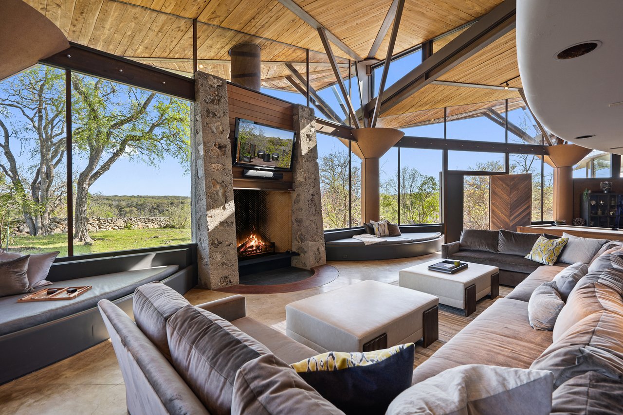 Family room with a native stone fireplace, branching steel tree columns and a wall of windows to the hill country, architect John Covert Watson.