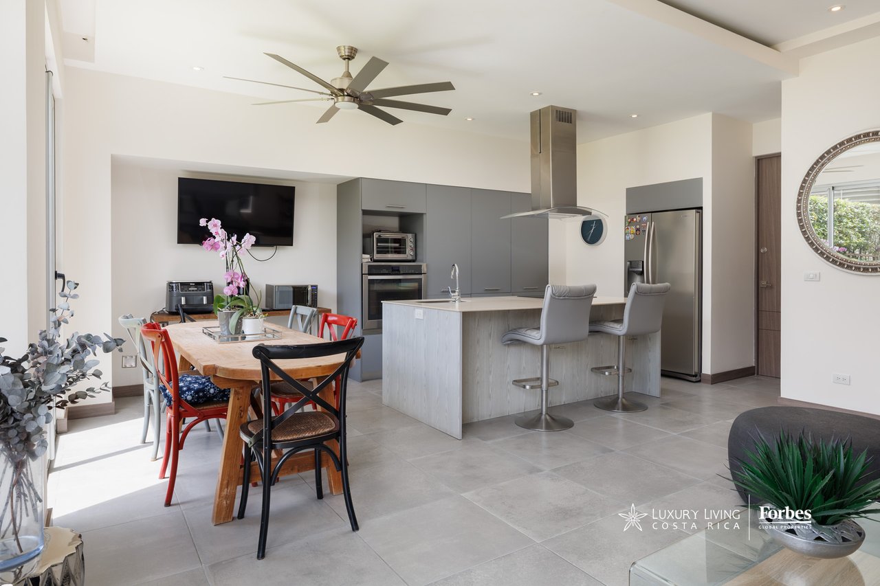 Open-plan kitchen and dining area with gray cabinetry, island seating, and a wooden table.