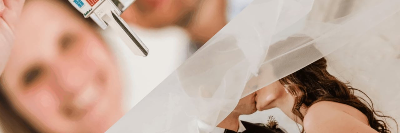 Newlyweds kiss beneath a veil as a hand holds house keys above them.