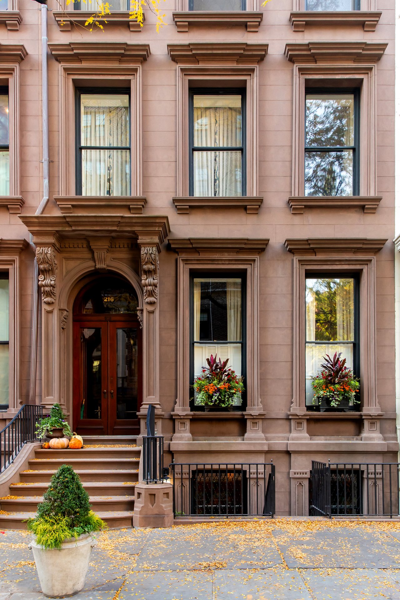 Brooklyn brownstone townhouse decorated for autumn, featuring pumpkins on the stoop, colorful window boxes, and fallen leaves on the sidewalk.