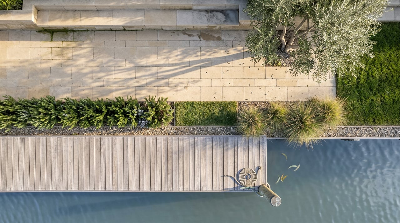 Stone patio, rosemary hedge, weathered dock, and coiled rope on a bronze cleat beside water.