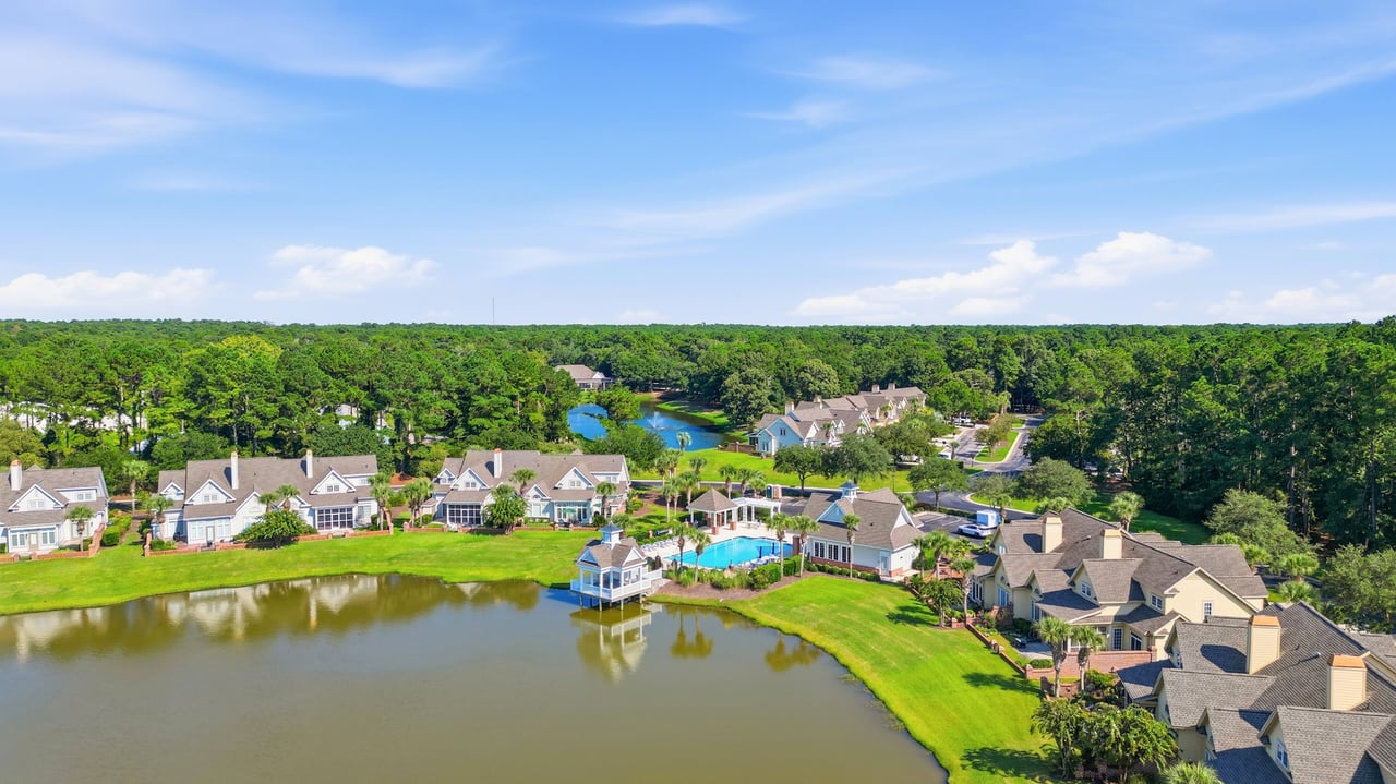 Huntington Lake Villas homes surrounding a lake, with a community pool and wooded horizon.