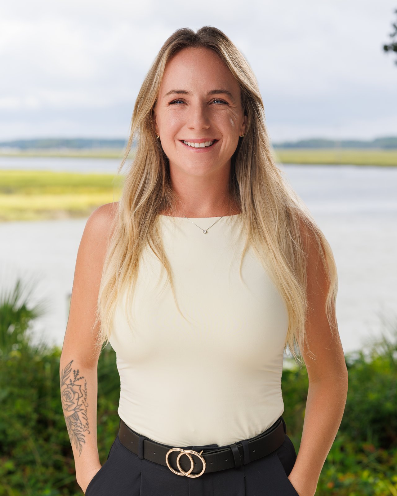 Chelsea Lewis, smiling sales agent with long blonde hair, standing before a coastal marsh.
