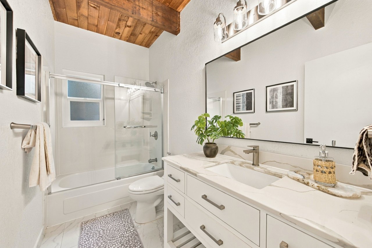 Bathroom with a glass-enclosed tub, white double vanity, and wood-plank ceiling.