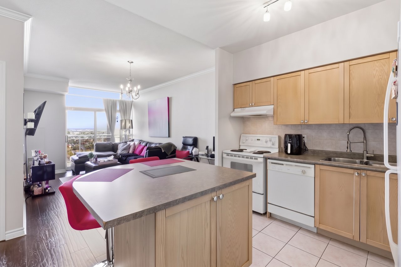 Open-plan penthouse kitchen with a large island, light wood cabinets, and a living room overlooking the city.