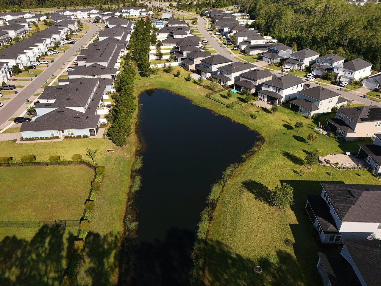 Aerial view of homes around a neighborhood pond, with trees lining the edge.
