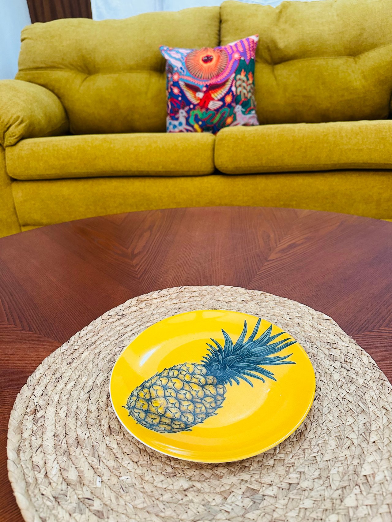 Living room with a mustard-yellow sofa and pineapple-decorated plate on a wood coffee table.