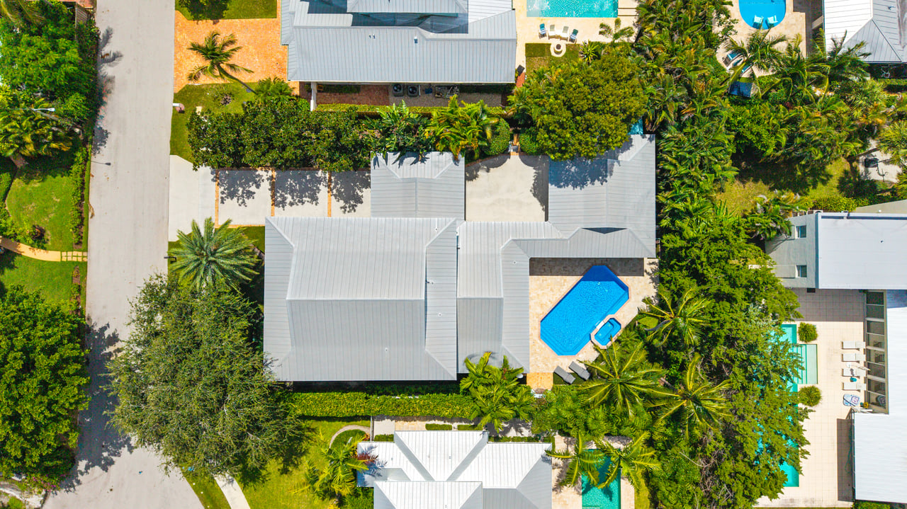 Aerial view of a home with a bright blue pool and dense tropical landscaping.