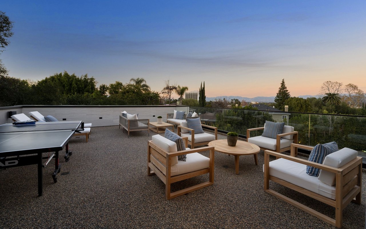 Rooftop terrace with lounge seating and a ping-pong table overlooking distant mountains at dusk.