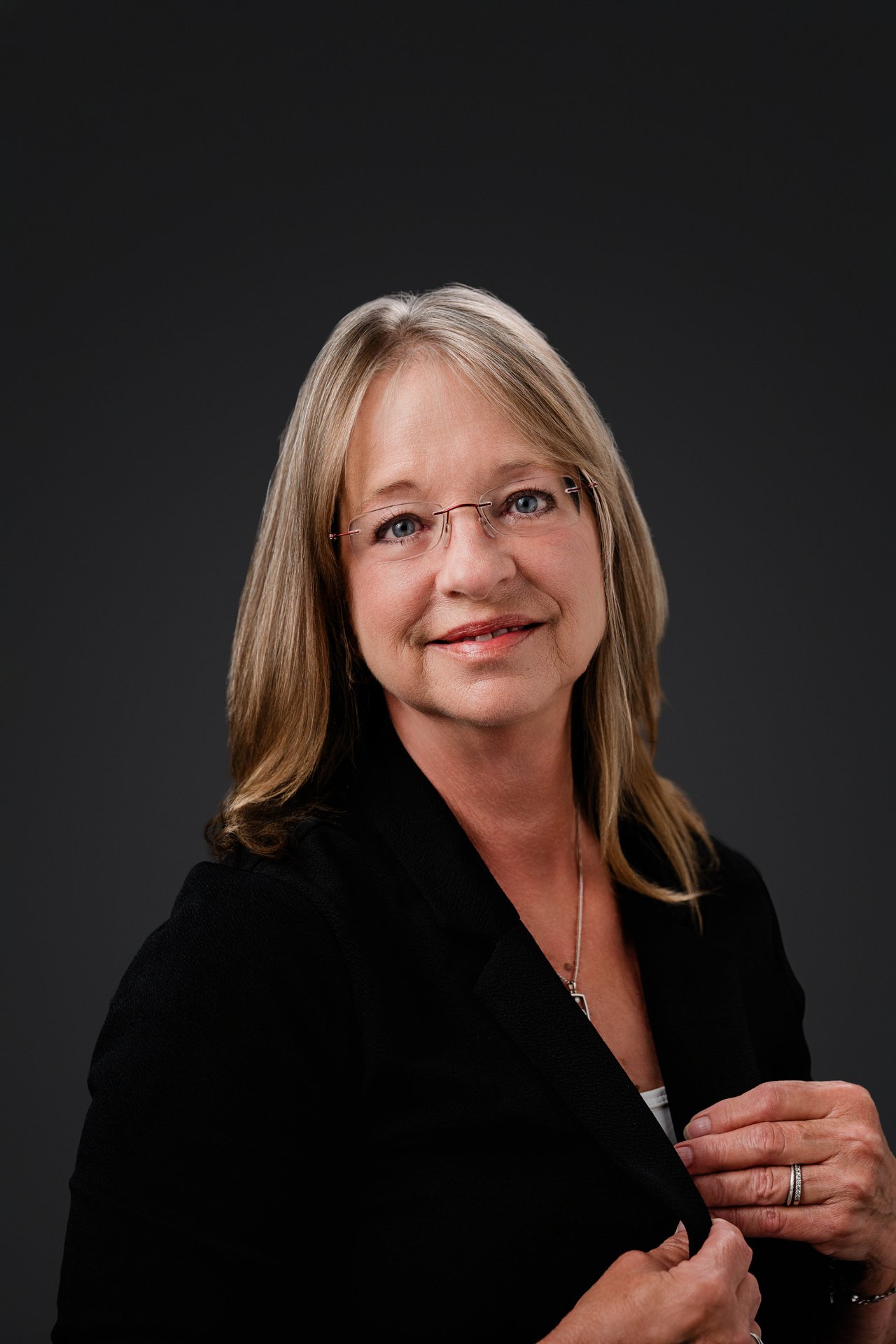 Angela Fulton wearing glasses and a black blazer against a dark background.